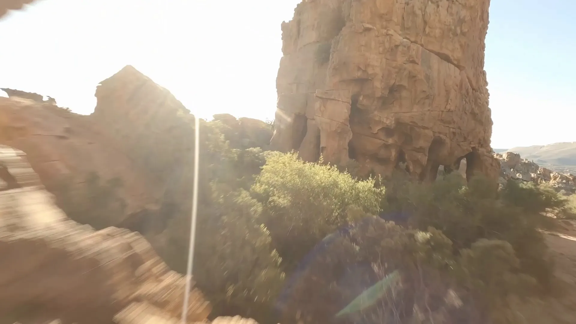 FPV drone diving past a sandstone cliff, sun flaring behind